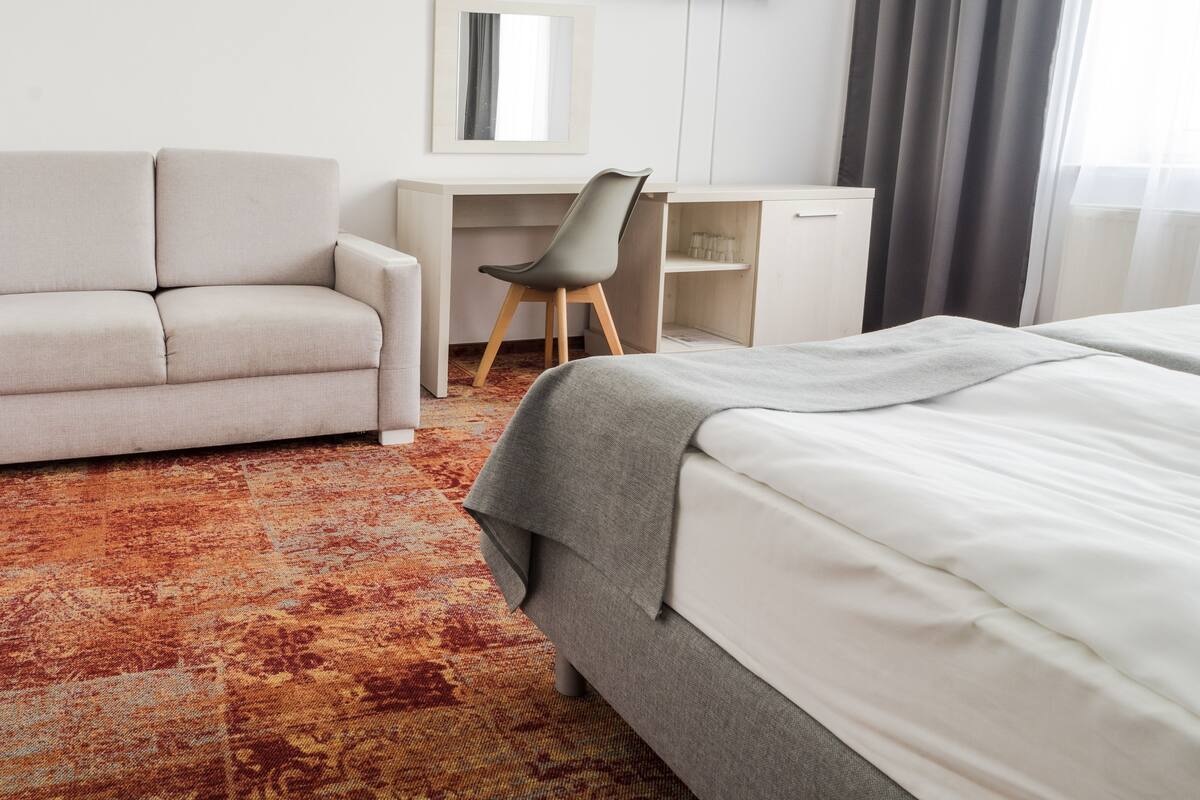 A hotel room with a bed, a sofa, a desk, a chair, a TV, and a patterned carpet.
