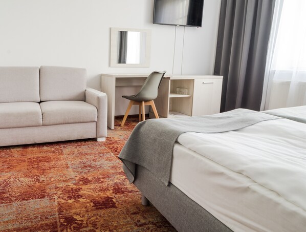 A hotel room with a bed, a sofa, a desk, a chair, a TV, and a patterned carpet. - Hotel Warmia Spa (Braniewo)