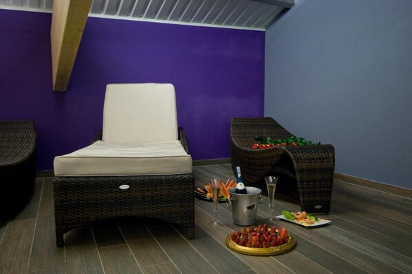 A room with a wicker chair, a cushioned bench, a small table with a drink and snacks, and a wicker basket with flowers. - Hotel Warmia Spa (Braniewo)