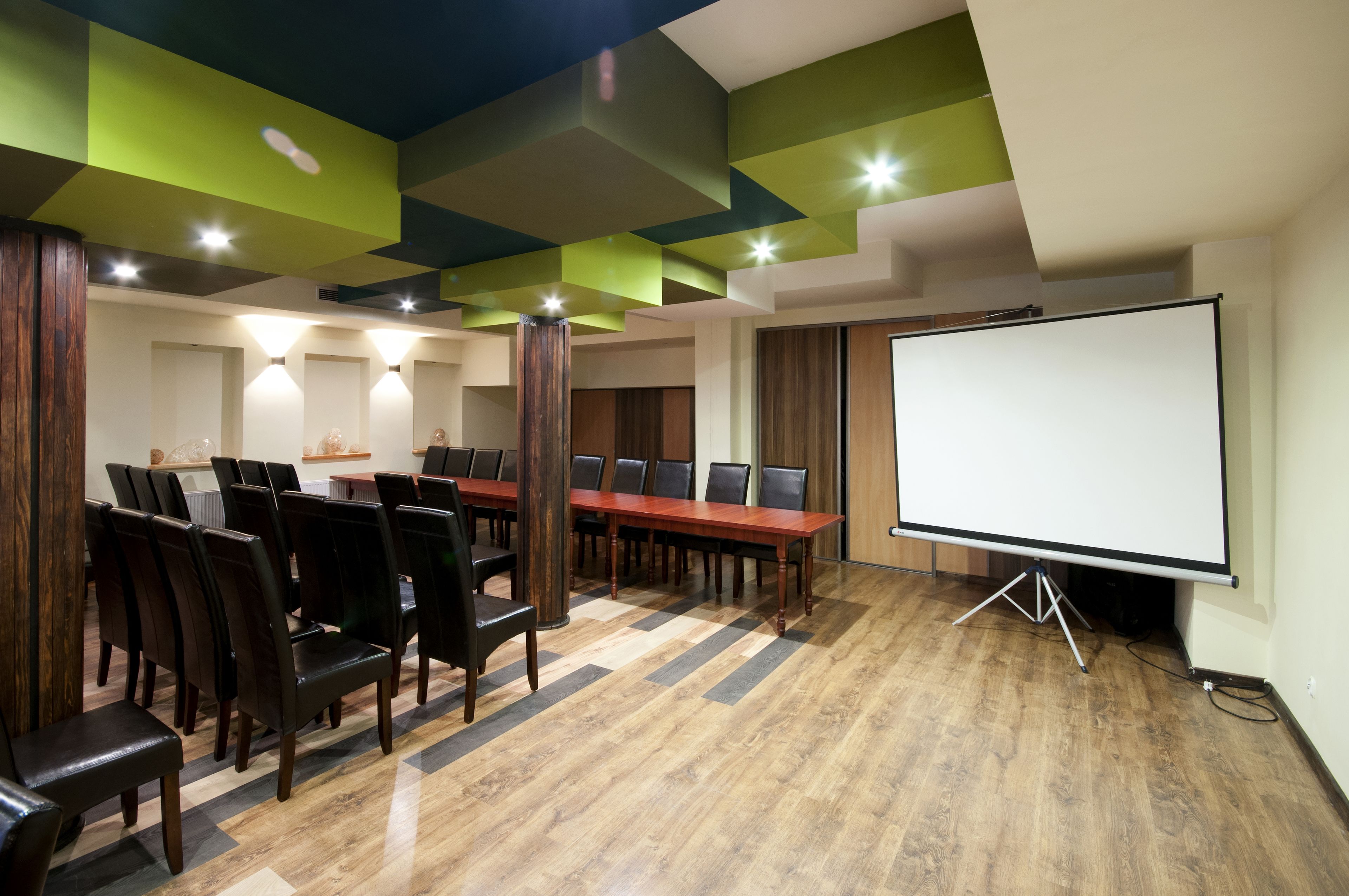 A conference room with a long table, chairs, a projector screen, and a wooden floor.