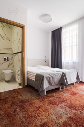 Un dormitorio con cama, inodoro y ventana con cortinas.