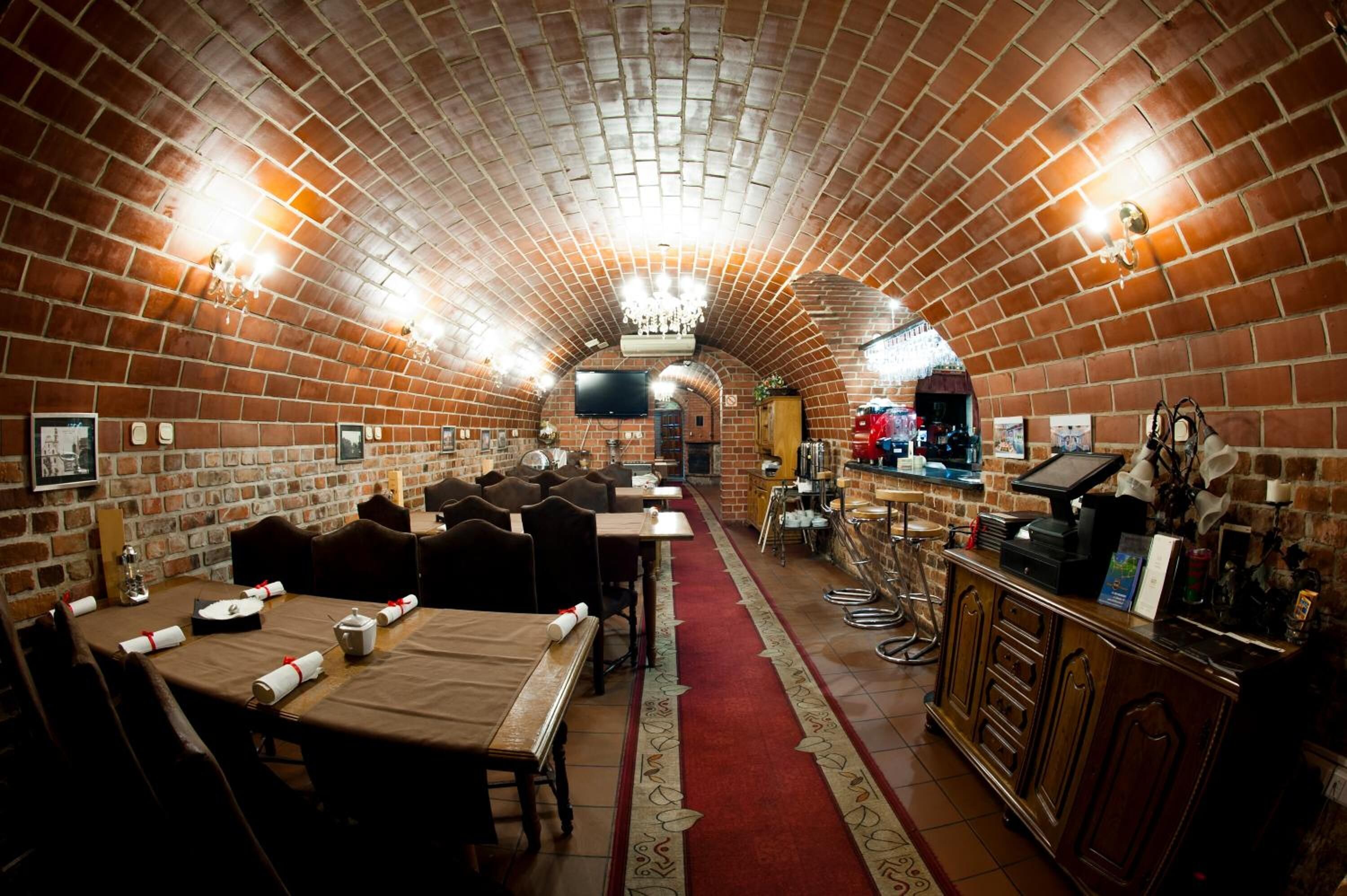 Un restaurant aux murs de briques, avec des tables dressées pour le service, un coin bar et un écran de télévision.