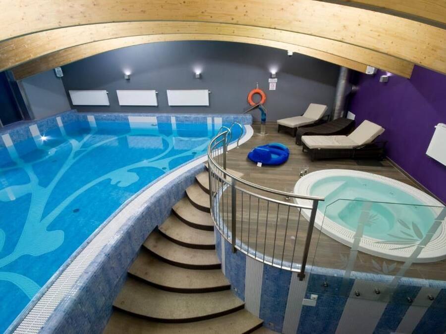 Una piscina interior con diseño azul, un jacuzzi y una escalera que lleva a la piscina.