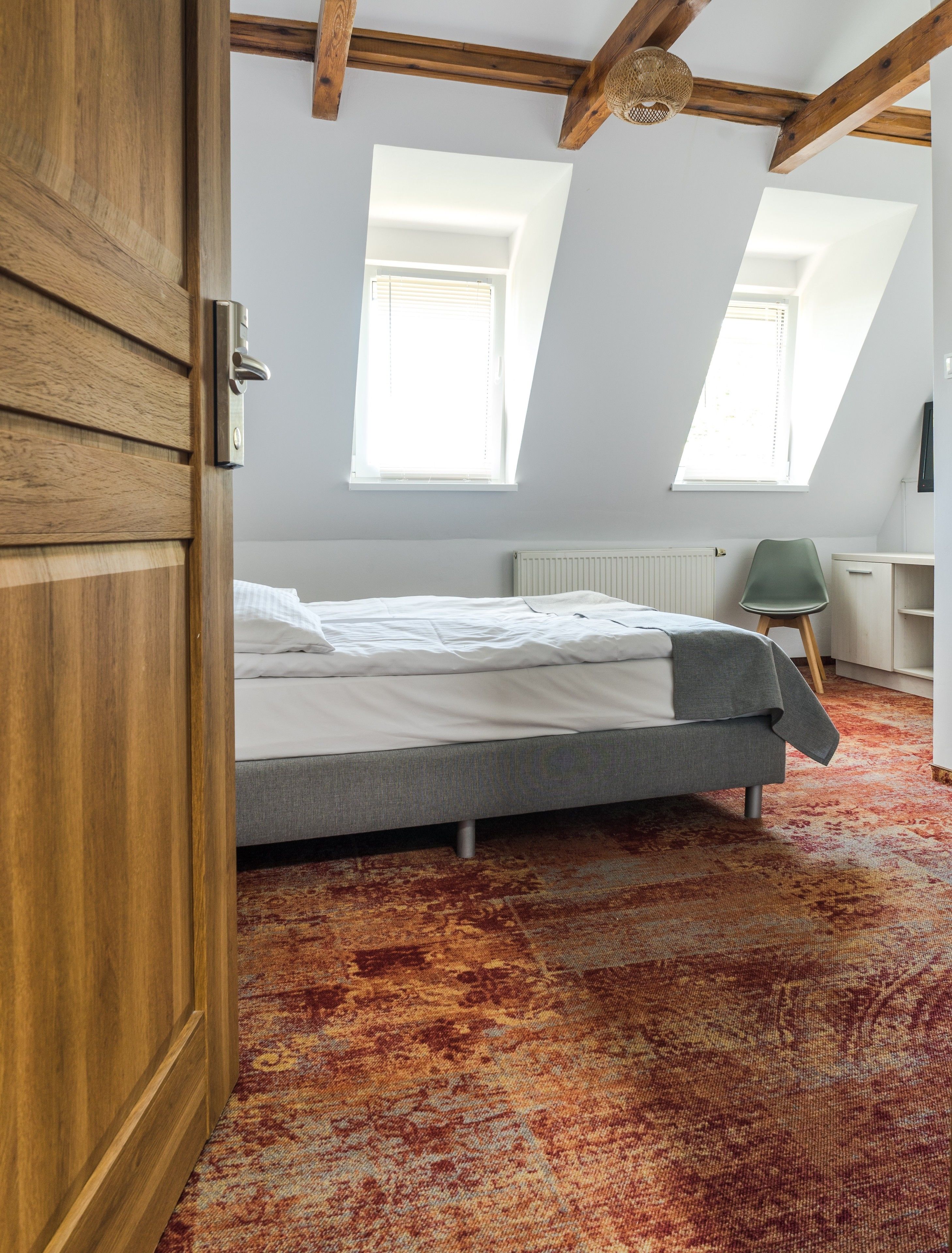 A bedroom with a bed, a chair, and a desk. There are skylights and a radiator.