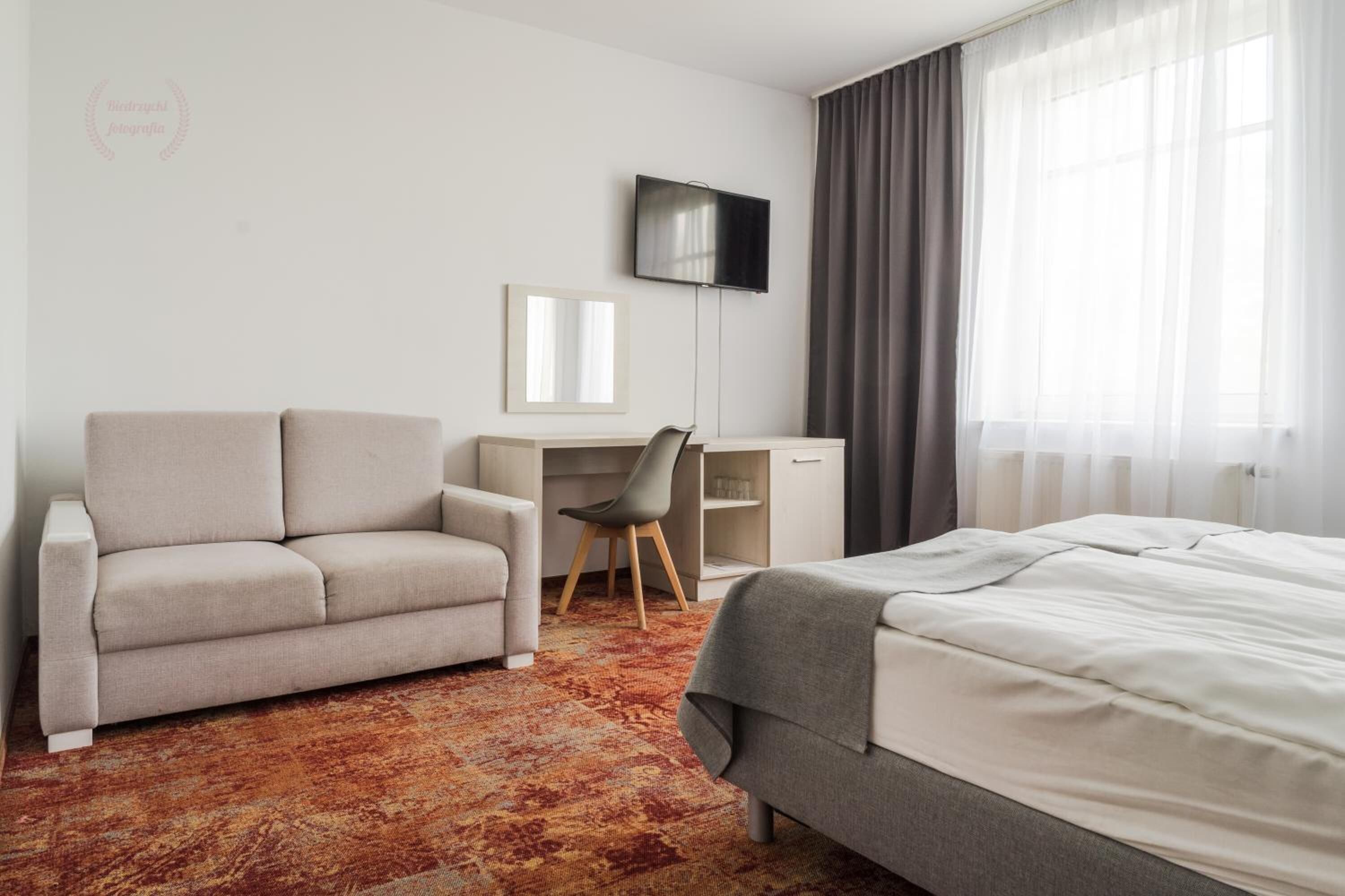 A hotel room with a bed, a sofa, a desk, and a TV.