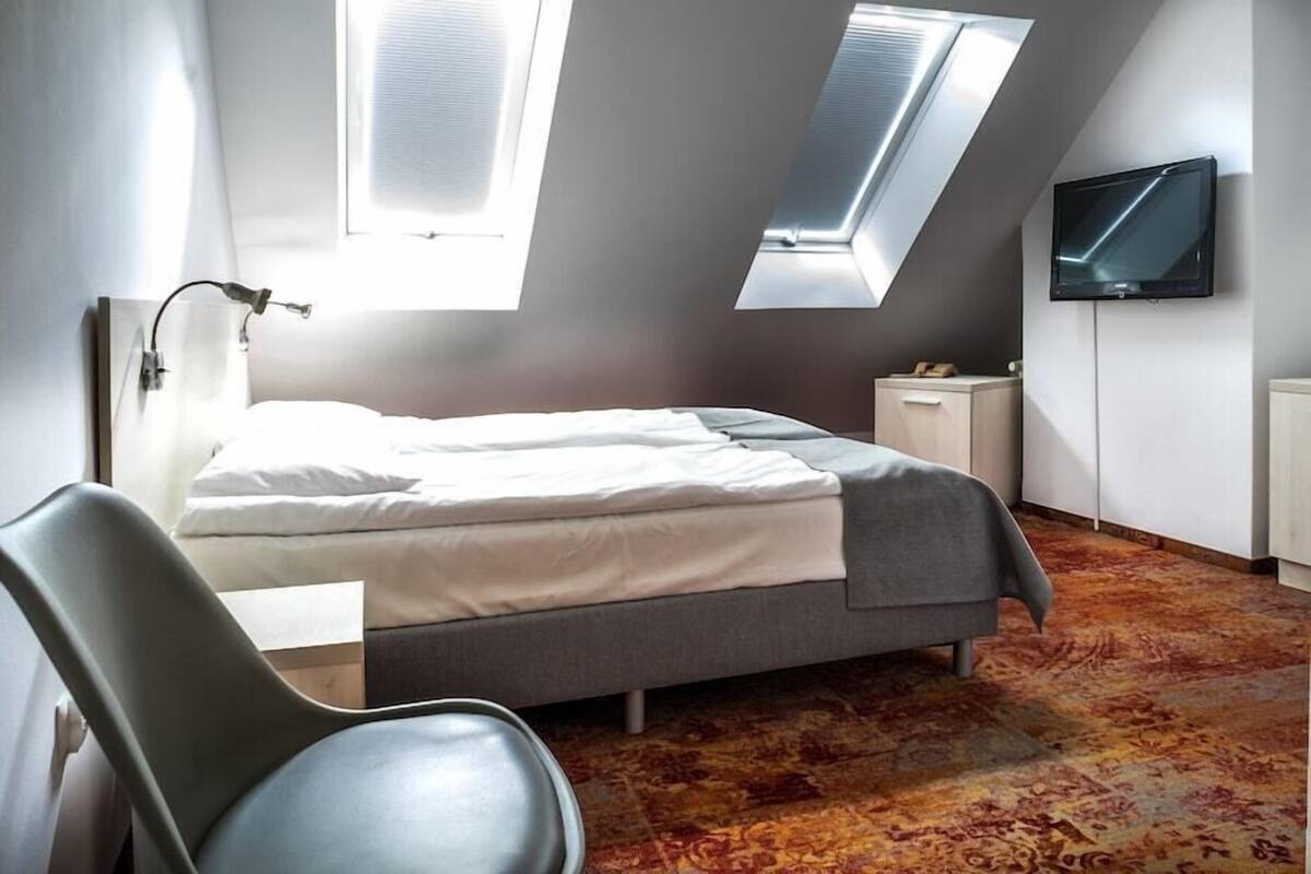 A bedroom with a bed, a chair, a TV, and skylights.