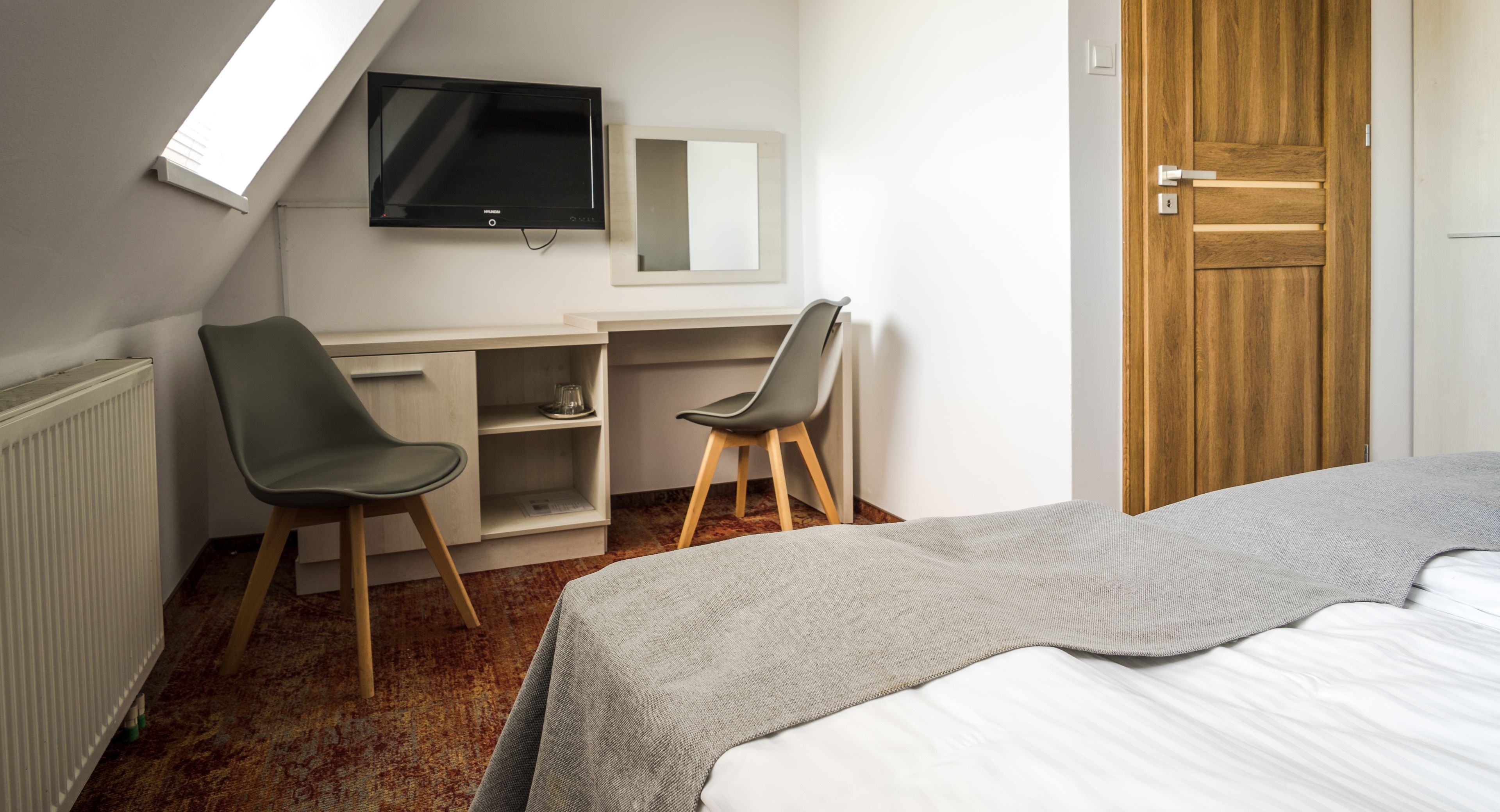 A bedroom with a bed, a desk with two chairs, a TV, and a wooden door.