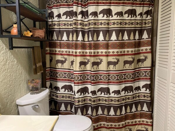 A bathroom with a shower curtain featuring animal patterns, a toilet, and a shelf with decorative items.