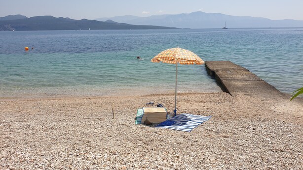 Una playa de guijarros con una sombrilla y un banco de madera.