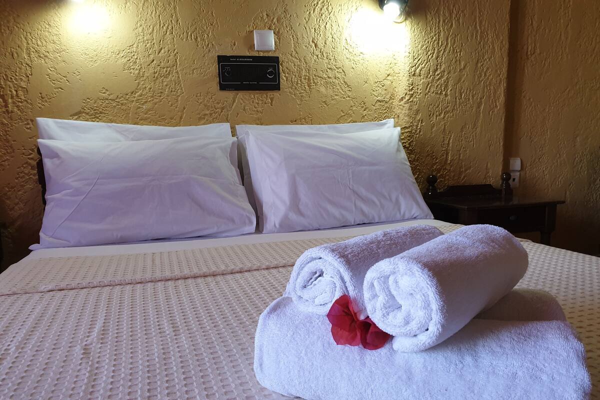 Hotellihuone, jossa on sänky, tyynyjä, ohjauspaneeli ja yöpöytä.