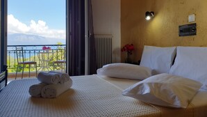 Habitación de hotel con una cama, vistas a montañas, un balcón con sillas y un florero con flores.