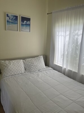 A bedroom with a bed, two framed pictures on the wall, and a window with curtains. - Baldwin Camp Rental Properties House #2, is located in North Caicos, TCI (North Caicos)
