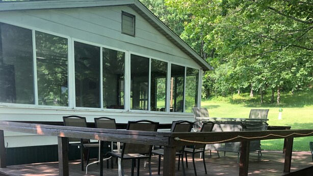 A covered outdoor deck with a table and chairs, surrounded by a wooden deck and gravel. - Wine Country Getaway (Burdett)