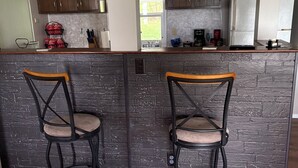 A kitchen with a central island, two bar stools, wooden cabinets, and a marble backsplash. - Wine Country Getaway (Burdett)