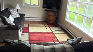 A living room with a sofa, a television on a stand, a window with curtains, and a patterned rug. - Wine Country Getaway (Burdett)