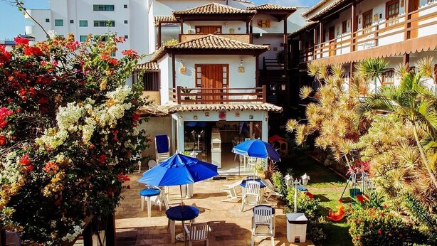 Un patio con mesas al aire libre, un edificio de techo de tejas y abundante vegetación.