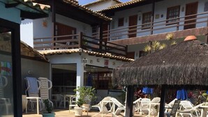 Una piscina con sillas de descanso y una sombrilla de paja, rodeada por un edificio con balcones.