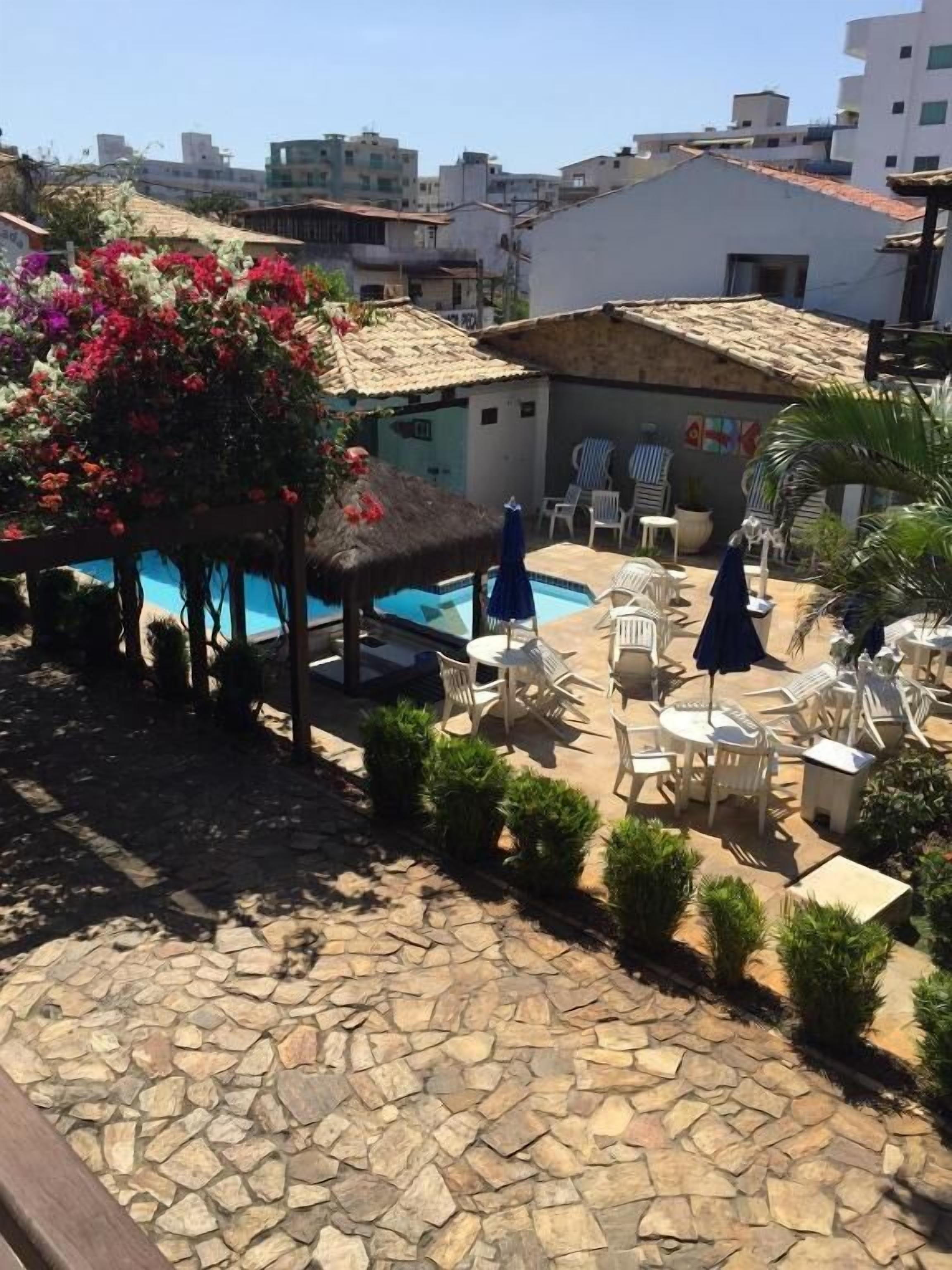 A pool area with lounge chairs and umbrellas, surrounded by stone flooring and greenery.