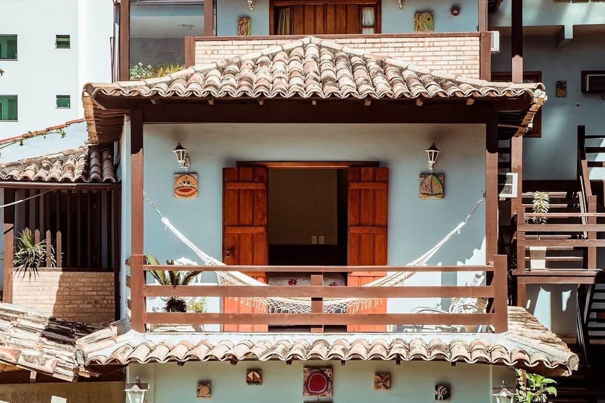 Um edifício de vários andares com varanda, persianas de madeira e telhado de telhas.
