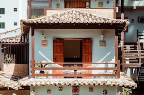 Un edificio de varios pisos con un balcón, contraventanas de madera y un tejado de tejas.