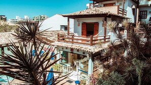 Un edificio de varios pisos con balcón, piscina y jardín con palmeras.