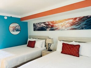 A hotel room with two beds, a round mirror, a wall painting, and a nightstand with a lamp.