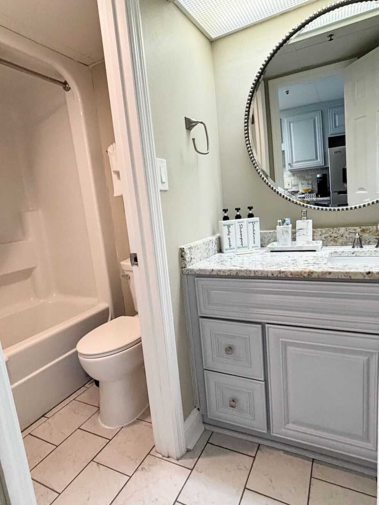 A bathroom with a bathtub, toilet, vanity with a mirror, and toiletries.