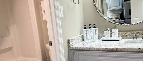 A bathroom with a bathtub, toilet, vanity with a mirror, and toiletries.