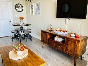 A dining area with a wooden table and chairs, a wooden cabinet with decorative items, and a wall-mounted TV.