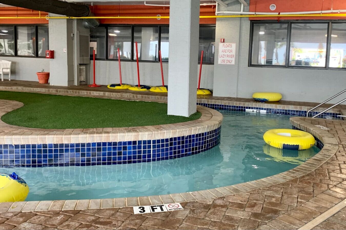 Una piscina interior con un indicador de profundidad de 3 pies, dispositivos de flotación amarillos y un letrero que indica 'Los flotadores son solo para el río lento'.