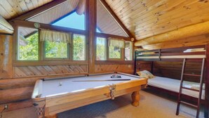 Una habitación acogedora con mesa de billar, literas y ventanas amplias que dan a zonas verdes.