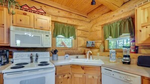 Una cocina compacta con armarios de madera, microondas, estufa, lavabo y lavavajillas.