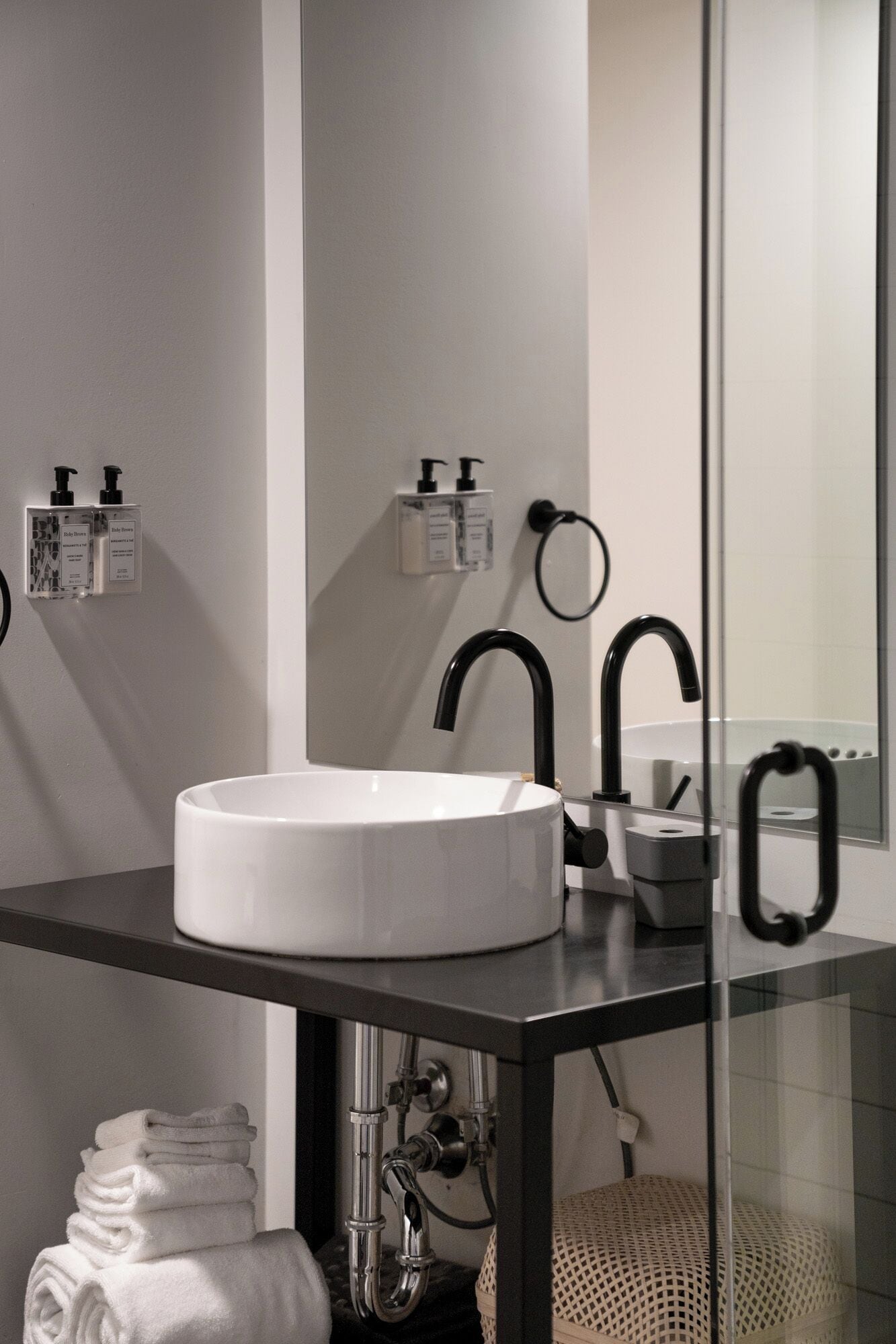 A modern bathroom with a white sink, black faucets, and two soap dispensers on the wall.