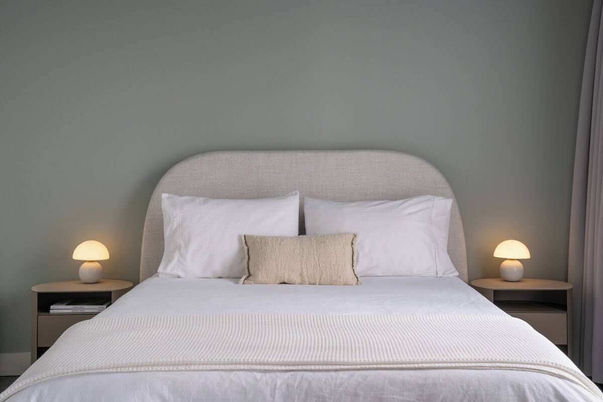 A neatly made bed with white linens and two bedside lamps.