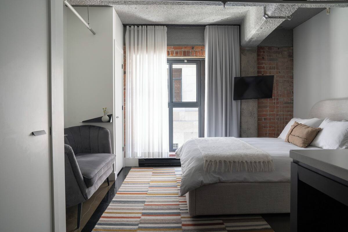 A modern bedroom with a bed, a desk, a TV, and a window with curtains.