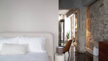 Un dormitorio con cama, una silla, un aparador y vistas a una zona de cocina.