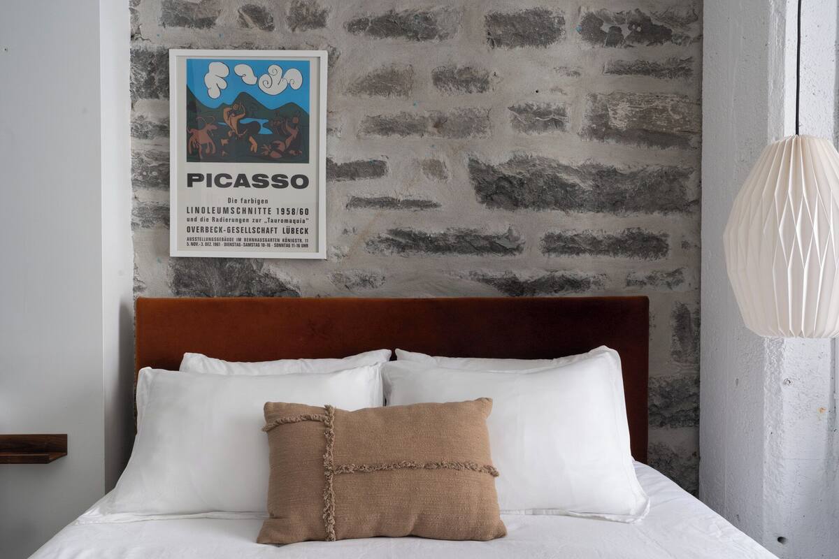 A bed with white linens and a brown pillow, a wooden headboard, and a poster on the wall.