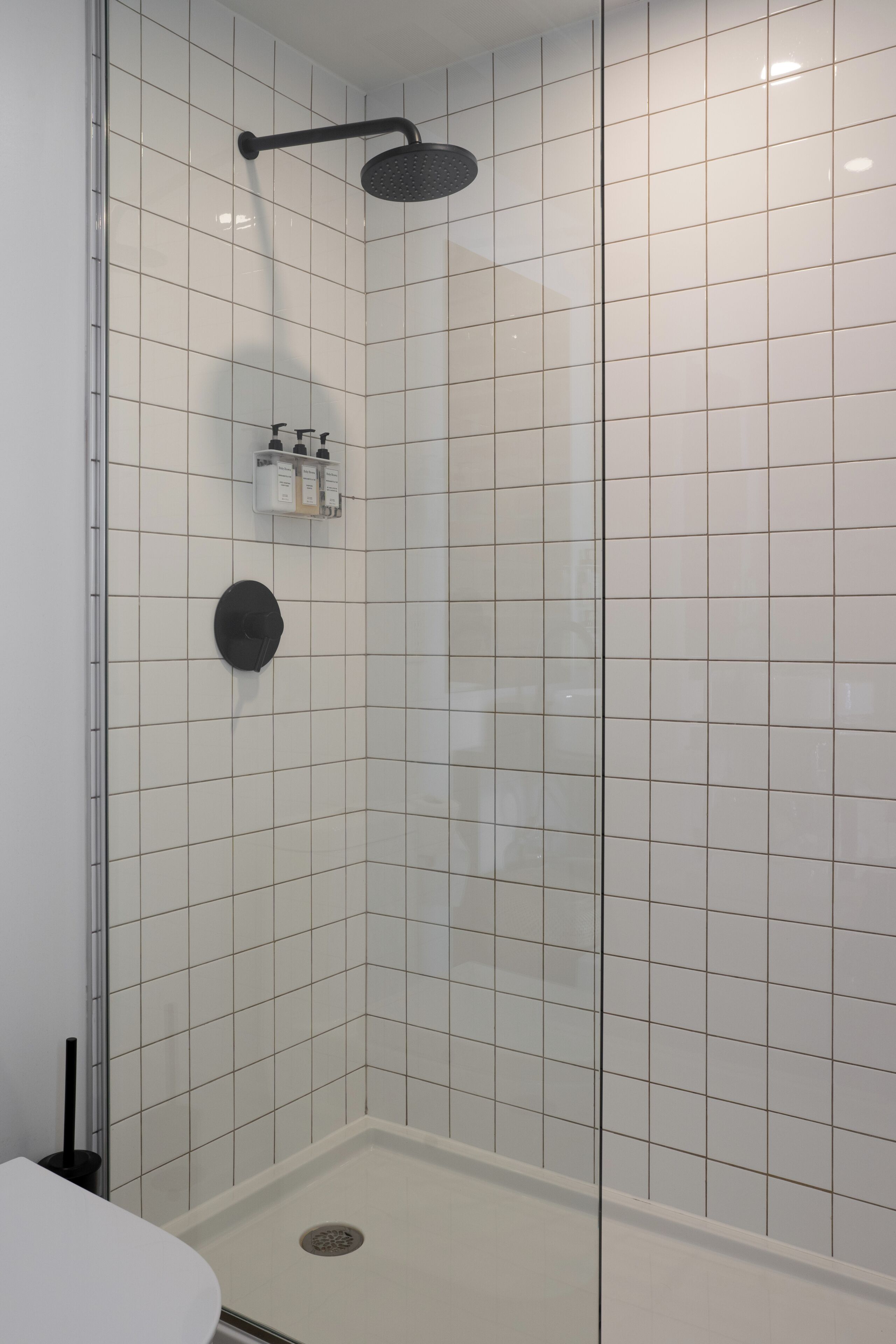 A shower with a glass door, a handheld showerhead, and a control panel.