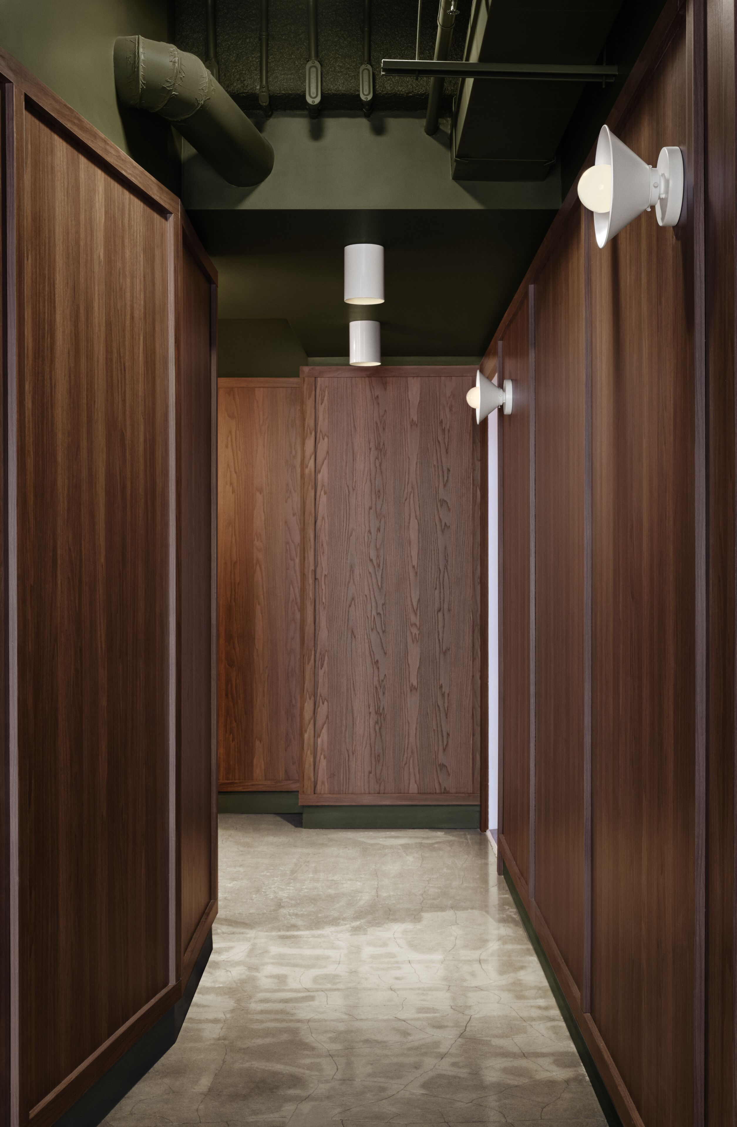 Un couloir avec des lambris en bois, un sol carrelé et des luminaires fixés au mur.