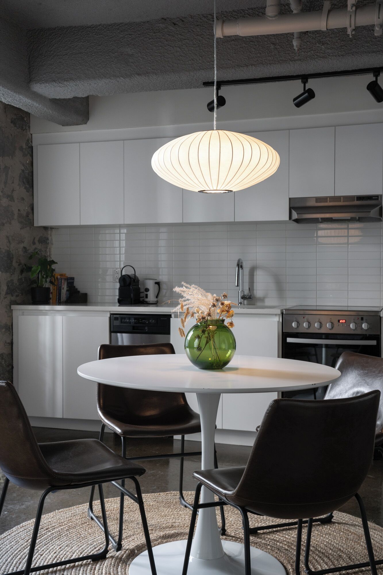 A modern kitchen with white cabinets, a stainless steel range hood, and a dining area with a white table and black chairs.