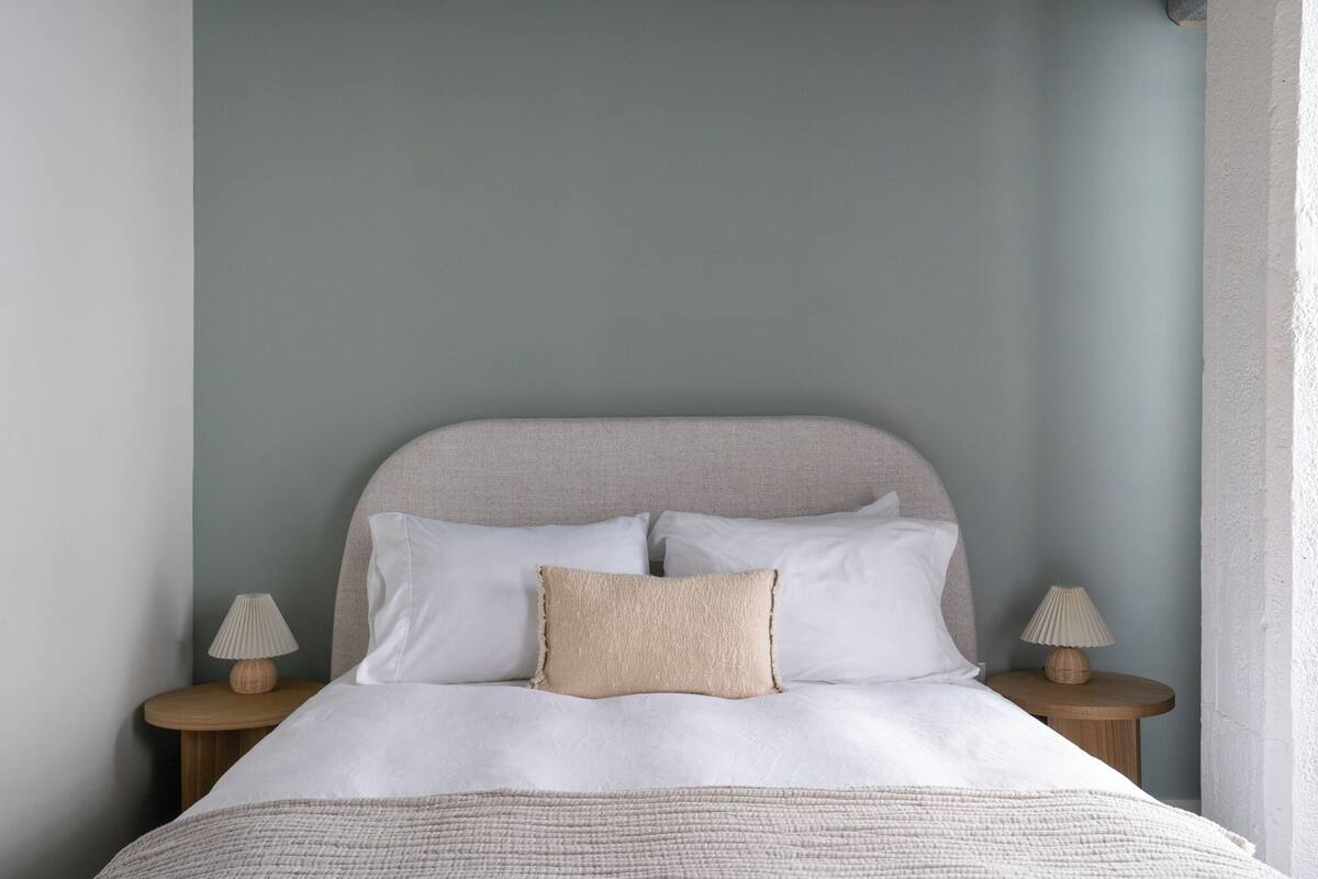A bed with a grey headboard, white bedding, and two bedside tables with lamps.