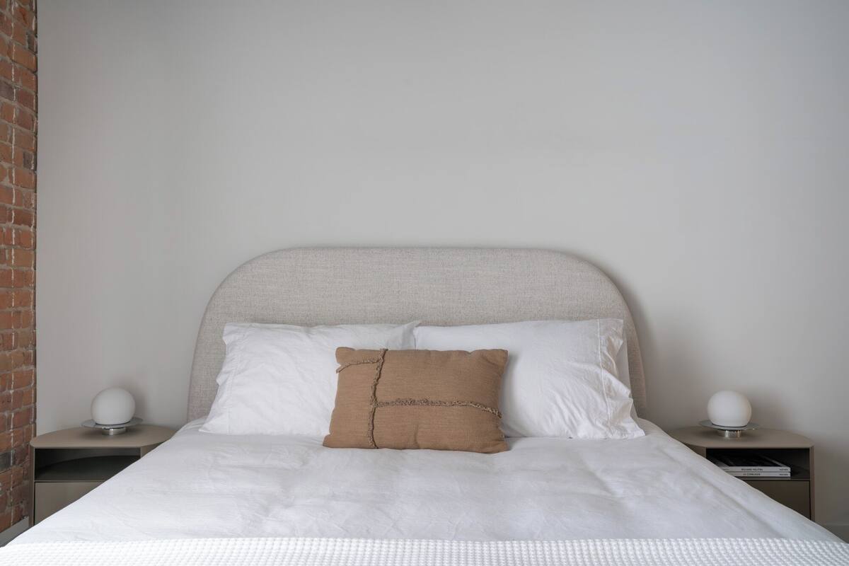 A neatly made bed with a white duvet and two pillows, one of which has a brown cover. There are two bedside tables with spherical lamps on them.