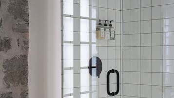 A shower with a glass door, a handheld showerhead, and a wall-mounted control panel.