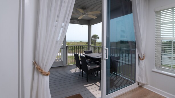 A covered outdoor area with a table and chairs, a ceiling fan, and a view of the beach.