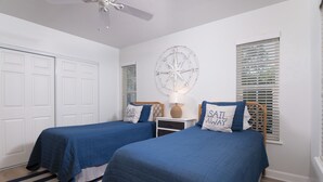 A bedroom with two beds, a ceiling fan, a wall clock, and a window with blinds.