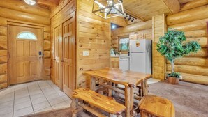 Interior de uma cabana de madeira com uma mesa de jantar, bancos, um frigorífico e um vaso de planta.