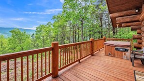 Um deck de madeira com hidromassagem e área de estar, com vista para uma paisagem arborizada.