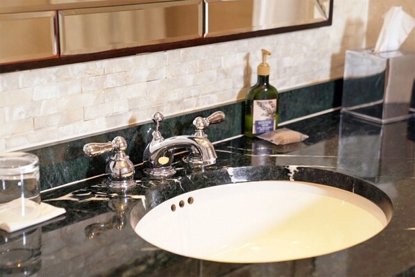 Une salle de bain avec un lavabo blanc, deux robinets chromés, un distributeur de savon et un boîte à mouchoirs.