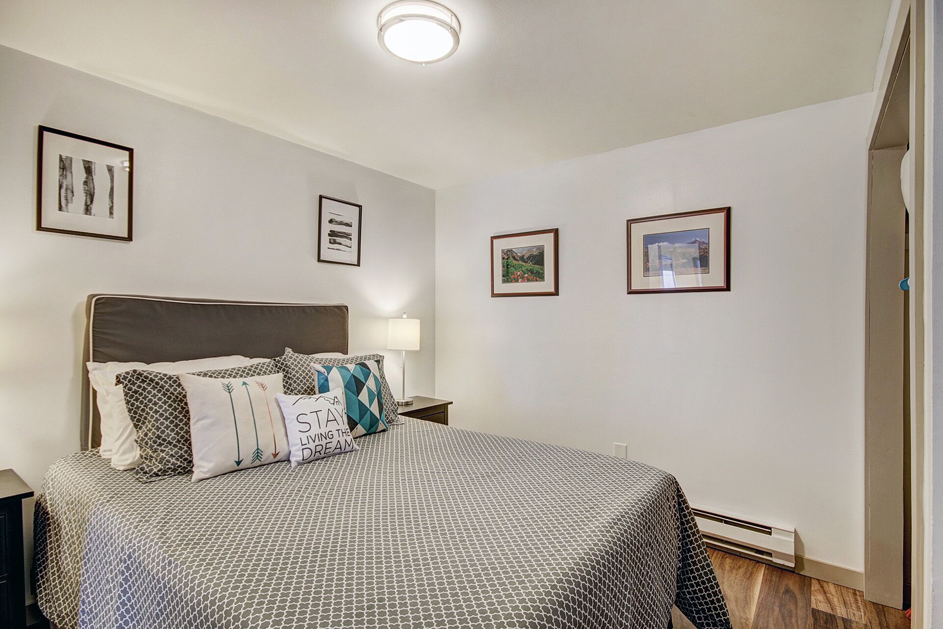 Ein Schlafzimmer mit Bett, Nachttisch, Lampe und gerahmten Bildern an der Wand.