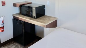 Une chambre d’hôtel comprenant un lit, une kitchenette équipée d’un four à micro-ondes et d’un petit réfrigérateur, un téléviseur à écran plat fixé au mur, et un détecteur d’incendie également fixé au mur.